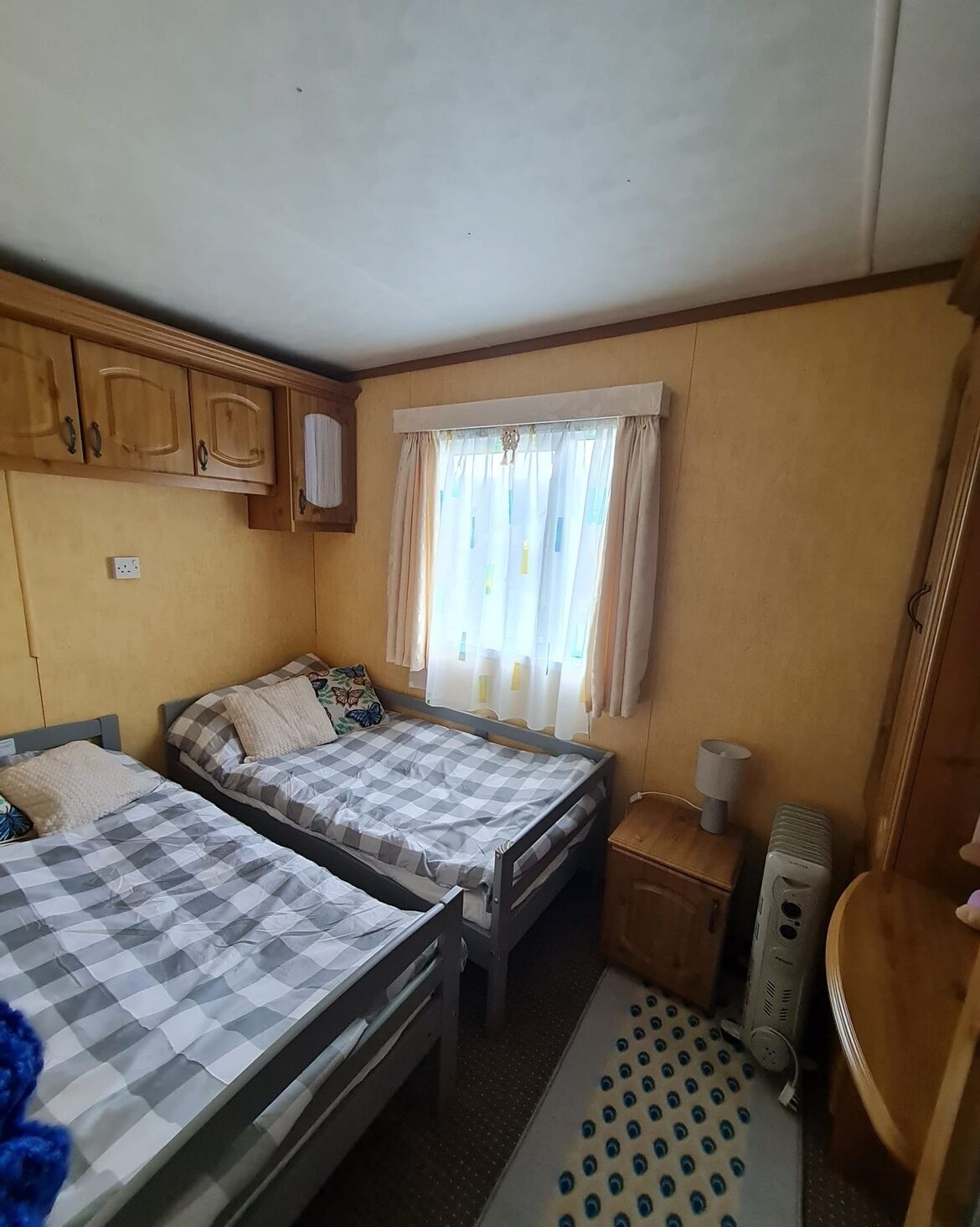 A compact room with two beds, a small table, a heater, and a window with curtains.