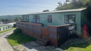 A green mobile home with a porch, a small deck, and a gas cylinder. - 2 Bed Caravan - Sleeps 6 - Pets - Pool - Parking (Aberystwyth)