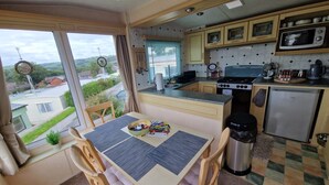 A compact kitchen with a dining area, a view of the outside, and basic amenities. - 2 Bed Caravan - Sleeps 6 - Pets - Pool - Parking (Aberystwyth)