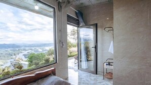 Un dormitorio con un ventanal grande, una cama y un baño con puerta de cristal.
