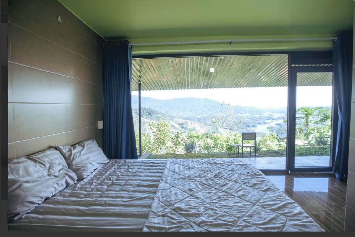 Une chambre dotée d’un grand lit, offrant une vue sur un paysage montagneux grâce à une porte-fenêtre coulissante, et comprenant un balcon avec un fauteuil.