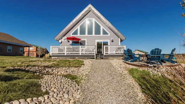 Une maison avec un porche à l’avant, un parasol rouge et un chemin de gravier menant à l’entrée.