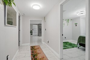 Un pasillo con suelo de baldosas blancas, un tapete floral y una puerta que da a un dormitorio con un tapete verde.
