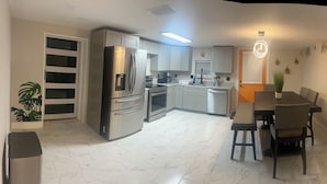 Una cocina moderna con electrodomésticos de acero inoxidable, un comedor con mesa y sillas, y un pequeño bote de basura.