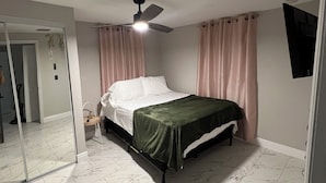 Un dormitorio con cama, ventilador de techo, espejo y televisor.