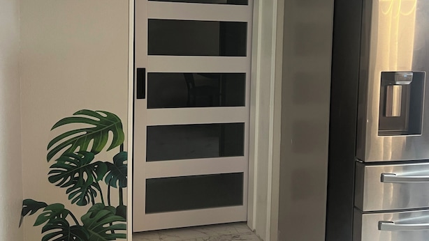 Una cocina compacta con refrigerador empotrado, una puerta blanca con paneles de vidrio y una planta en maceta.