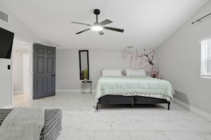 A bedroom with a bed, a ceiling fan, a window, and a door.