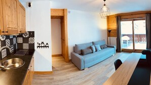 Un espace de vie compact comprenant un coin cuisine, un canapé, un coin repas et un téléviseur fixé au mur.