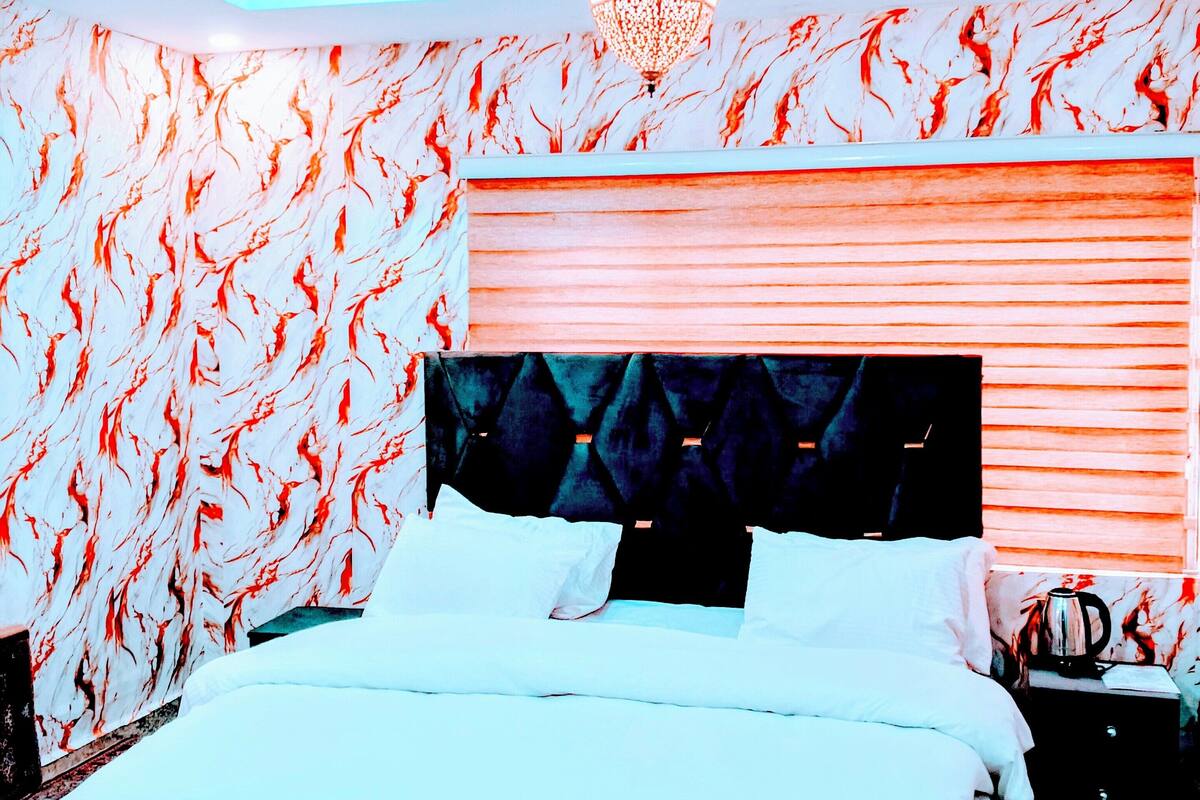 Une chambre à coucher avec un lit, une table de chevet, une lampe et un mur décoré d’un motif.