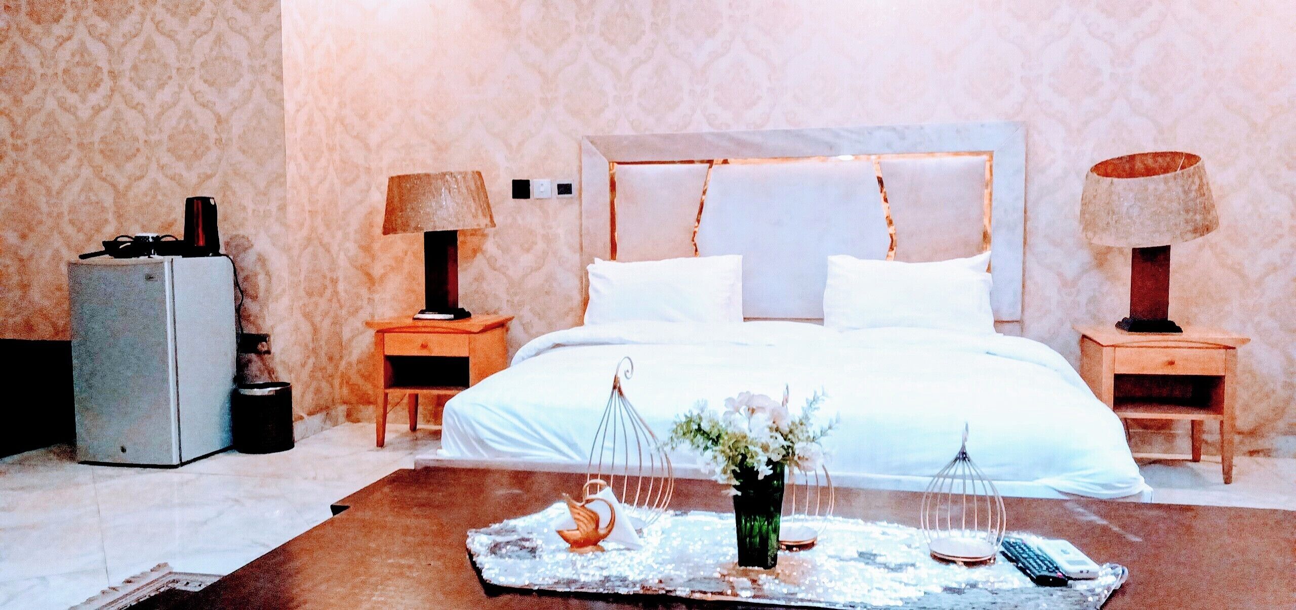 A hotel room with a large bed, two bedside tables, a nightstand, a dresser, and a coffee table with decorative items.
