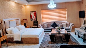 A well-lit hotel room with a bed, a sofa, a coffee table, and a TV.