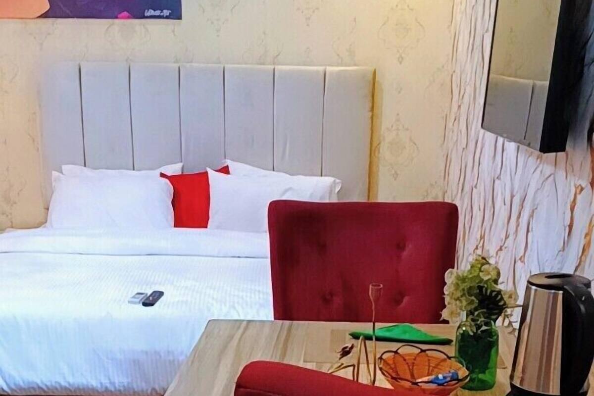 Une chambre d’hôtel avec un lit, une chaise rouge, une petite table, un téléviseur et un tableau décoratif.
