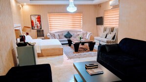 A modern living room with a bed, sofa, and armchair, a coffee table, and a TV.