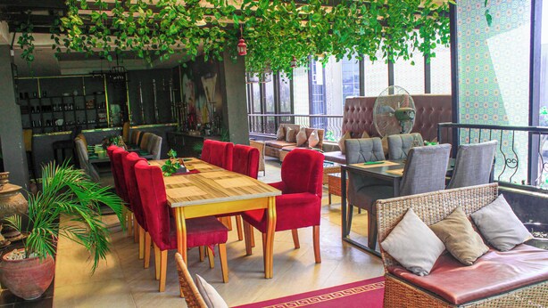 A restaurant with red chairs, a wooden table, and a wicker sofa with cushions.