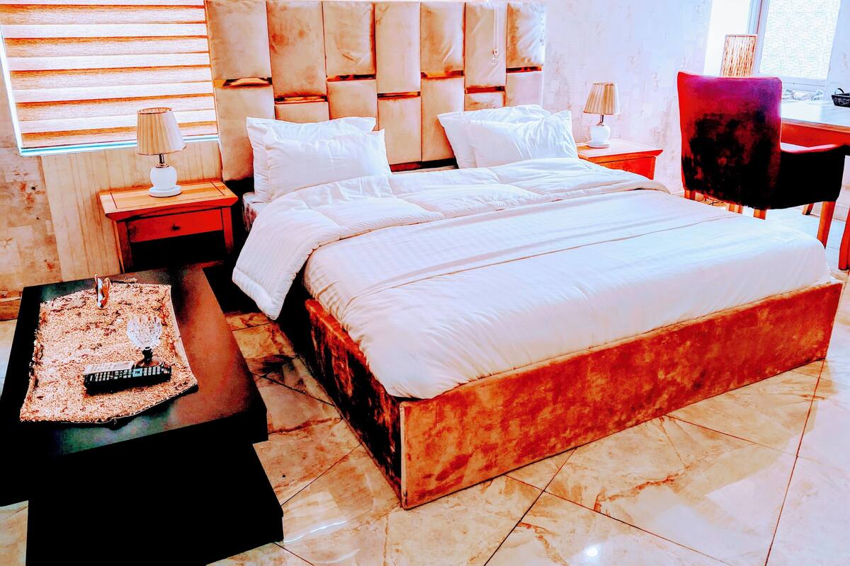 Une chambre moderne avec un grand lit, une table de chevet, une lampe et une chaise.