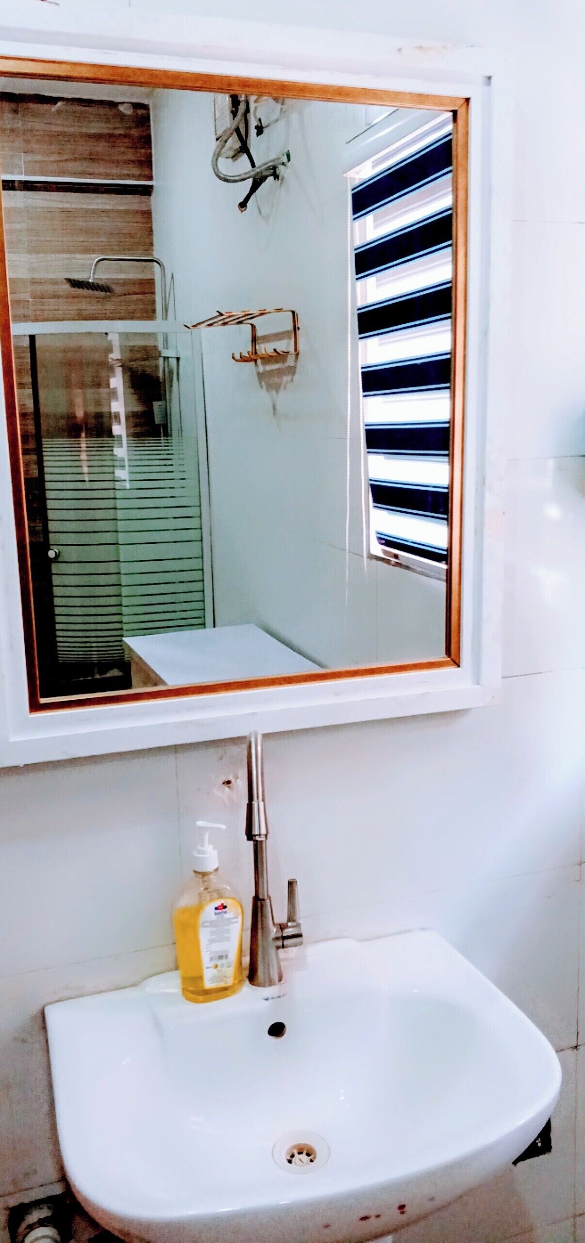 A bathroom with a white sink, a mirror, and a window with horizontal blinds.