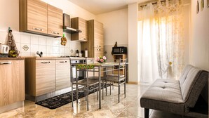 A modern kitchen with wooden cabinets, a dining area with chairs, and a grey sofa. - Vacation Home La Dolce Vita (Terrasini)