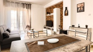 A modern living room with a sofa, a dining table with a placemat, a TV, and a fireplace. - Vacation Home La Dolce Vita (Terrasini)