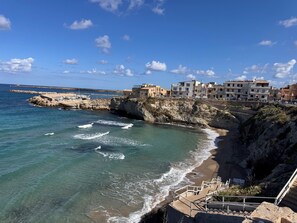 A coastal town with buildings along the cliffside, a sandy beach, and a rocky shoreline.