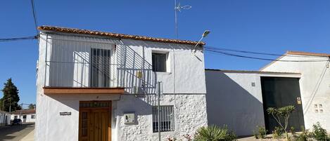 A two-story building with a white facade, a wooden door, and a small balcony.