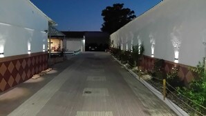 Een pad begrensd door witte muren met kleine lichtjes, dat naar een gebouw leidt met een zichtbare ingang en een overdekt gebied.