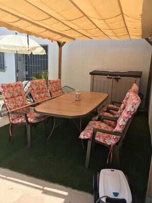 Un espace extérieur aménagé en patio, avec une table et des chaises en bois, une petite lanterne blanche et un coin salon abrité.