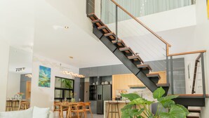Amplia sala de estar con una escalera moderna, una mesa de comedor y una planta grande en maceta.