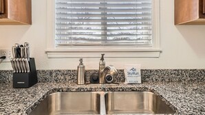A kitchen with a granite countertop, stainless steel sink, and a window with blinds. - Dover Court • 2BR Red Rocks Basecamp in Lakewood (Lakewood)