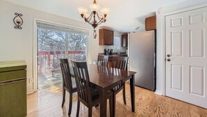A dining area with a wooden table and chairs, a chandelier, and a view through a glass door to a deck. - Dover Court • 2BR Red Rocks Basecamp in Lakewood (Lakewood)