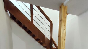 Un escalier avec des rampes en bois et un canapé noir dans une pièce dont le sol est recouvert de carreaux.