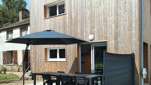 Une maison moderne en bois dotée d’un patio, d’un espace salon extérieur et d’un grand parasol.