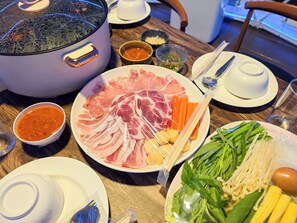 A dining table with a variety of food items, including a hot pot, plates of sliced meat, vegetables, and condiments. - 19 Degrees Resort (Sai Yok)