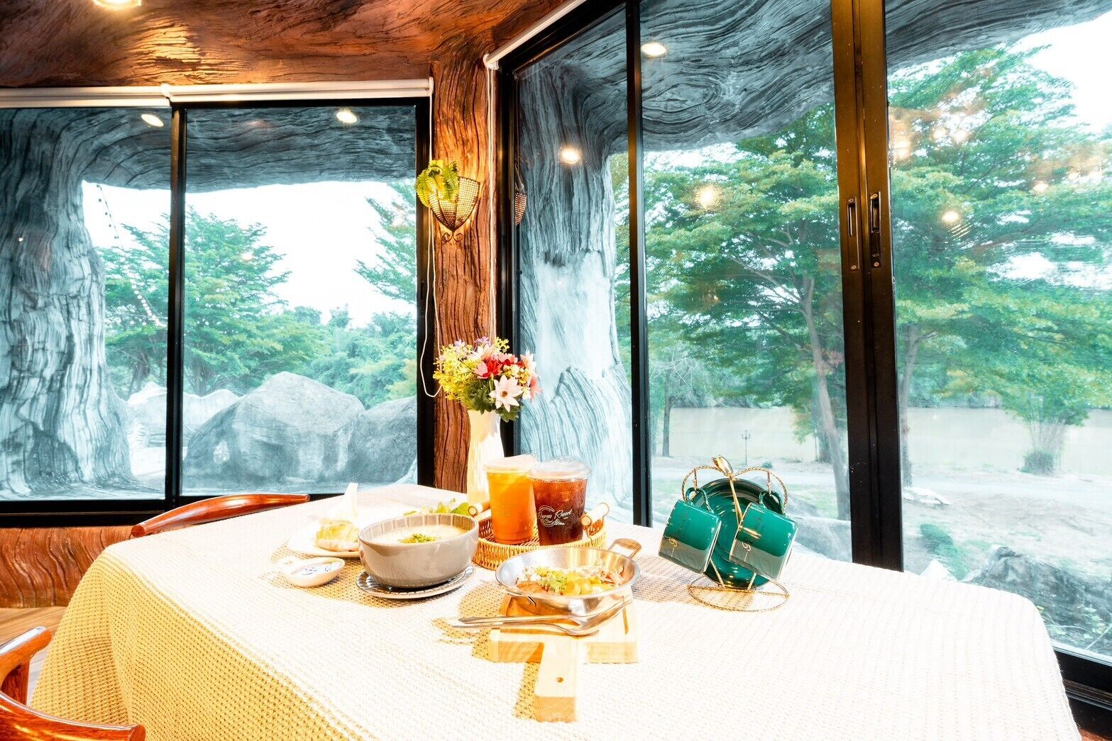 A dining table set with a vase of flowers, a glass of tea, and a green handbag.