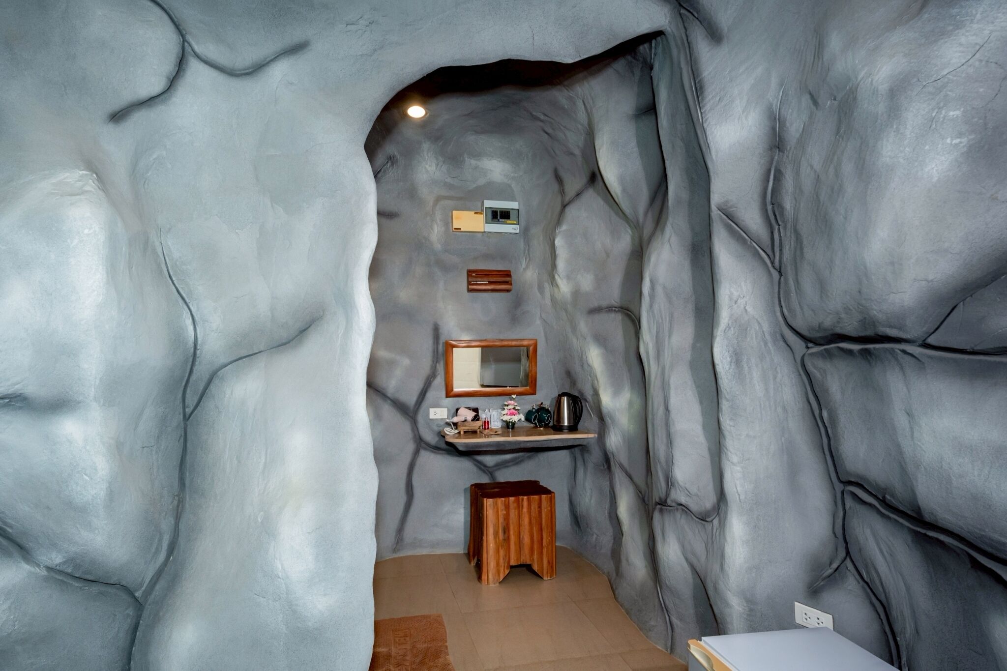 Um banheiro com design que lembra uma caverna, com pia, espelho e prateleira com artigos de higiene pessoal.