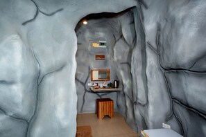 A bathroom with a cave-like design, featuring a sink, mirror, and shelf with toiletries. - 19 Degrees Resort (Sai Yok)