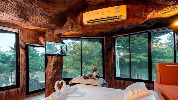 A treehouse bedroom with a large bed, a television, and a view of the forest.