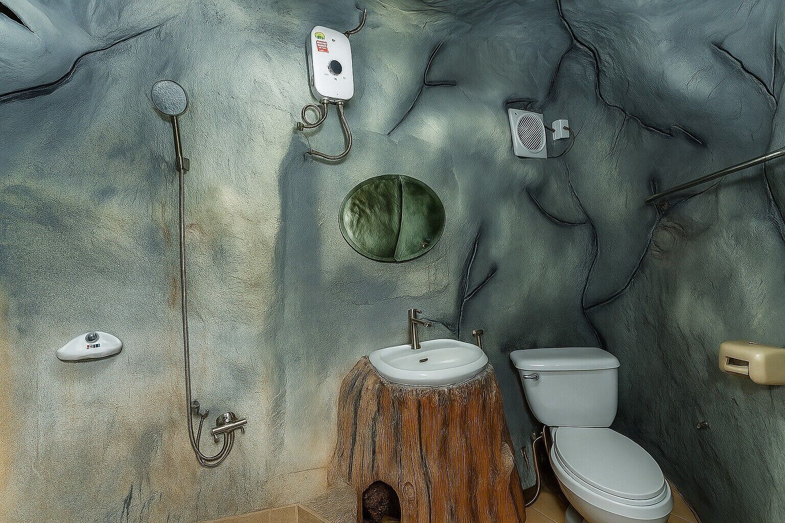 Une salle de bain au décor rustique, comprenant un tabouret en bois, un lavabo, des toilettes et une douche avec un flexible.
