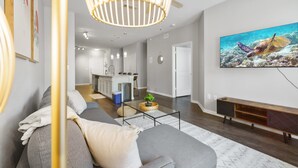 A modern living room with a grey sofa, a coffee table, and a painting of a sea turtle. - Bright 2BR Flat w/ Balcony + Pool | Walk to SoCo (Austin)