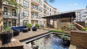 A rooftop garden with a wooden deck, seating area, and a small pond. - Bright 2BR Flat w/ Balcony + Pool | Walk to SoCo (Austin)