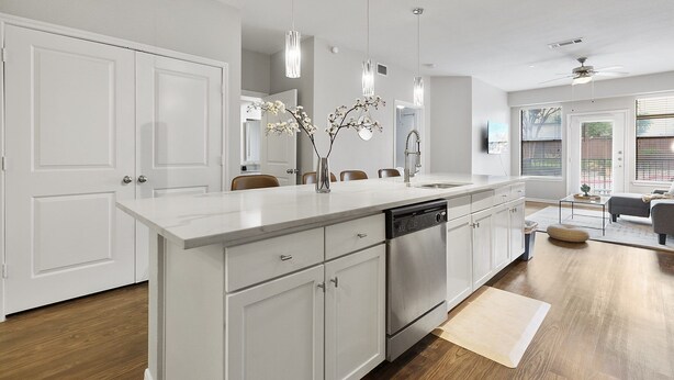 A modern kitchen with white cabinetry, a central island, stainless steel appliances, pendant lighting, and a view to the living area. - Bright 2BR Flat w/ Balcony + Pool | Walk to SoCo (Austin)