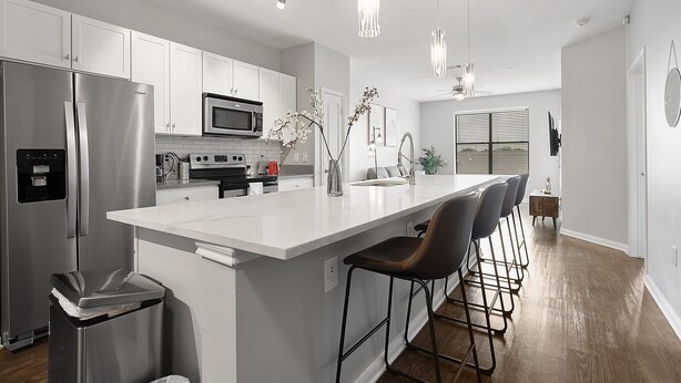 A modern kitchen with stainless steel appliances, a white island with bar stools, pendant lighting, and a view to the dining area. - Chic 1BR Retreat | Walk to SoCo, Pool & Wi-Fi (Austin)