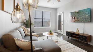 A modern living room with a sofa, a coffee table, a TV, and a ceiling fan. - Chic 1BR Retreat | Walk to SoCo, Pool & Wi-Fi (Austin)