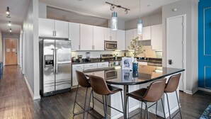 A modern kitchen with stainless steel appliances, a central island with bar stools, and pendant lighting. - Modern 2BR Loft w/ Pool + Balcony in Heart of SoCo (Austin)