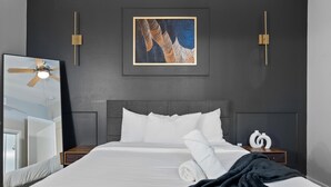 A hotel room with a large bed, a ceiling fan, a framed artwork, and a nightstand with a vase. - Modern 2BR Loft w/ Pool + Balcony in Heart of SoCo (Austin)