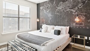 A modern bedroom with a world map mural, a large bed, a bench, and a hanging light fixture.