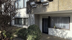 A modern building with a stone facade, large windows, and a paved entrance area with a small bush. - Cozy - Guest room (Notzingen)