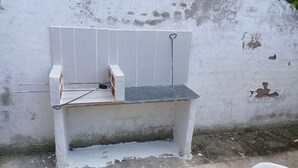 Um banco branco com estrutura metálica e assento de ripas em frente a uma parede desgastada.