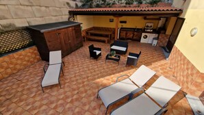 A patio area with tiled flooring, a wooden cabinet, a sofa, two chairs, a small table, and a washing machine.