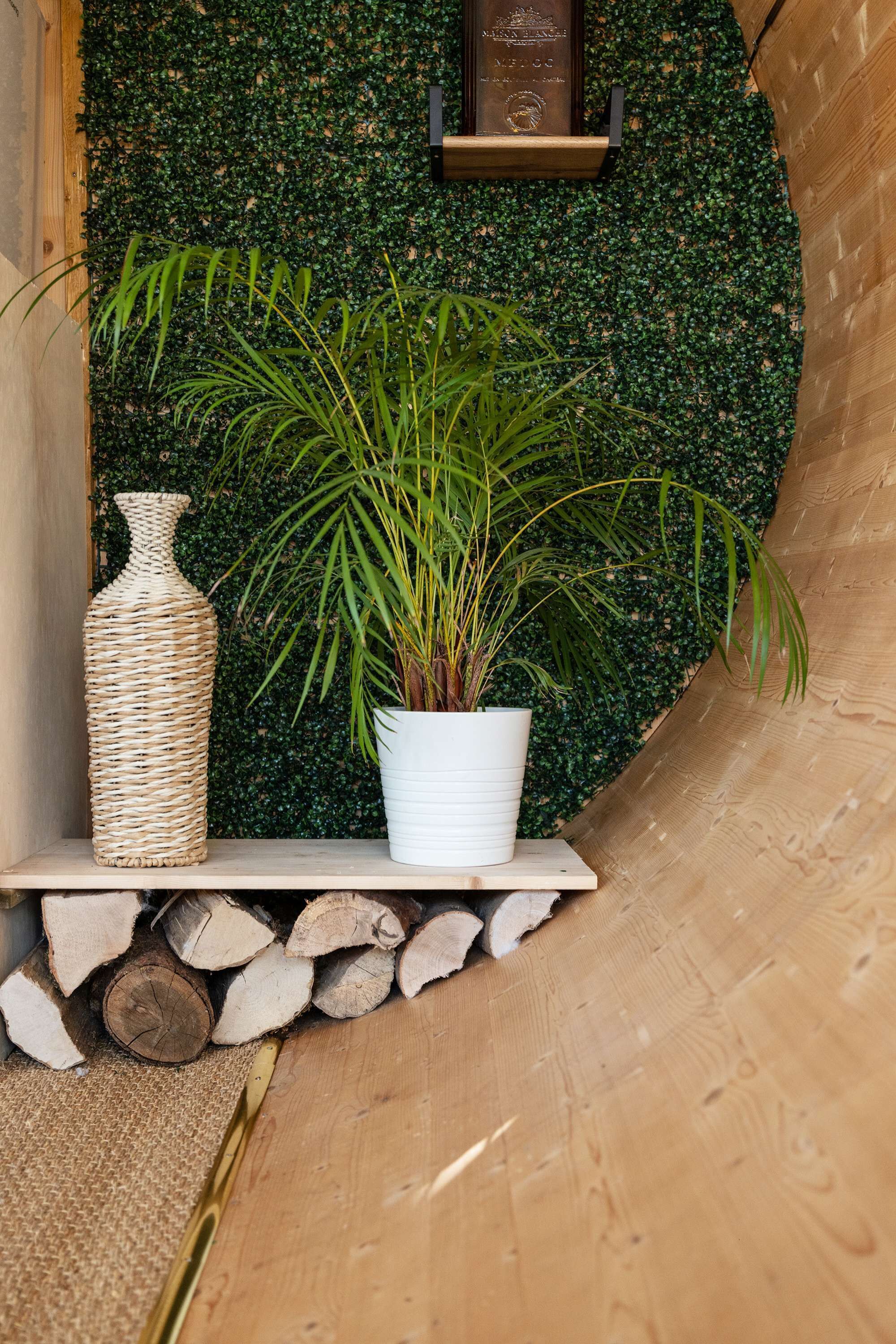 Une étagère avec un vase en osier et une plante en pot, le tout placé devant un mur vert.
