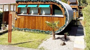 A unique, curved wooden building with large windows and a small garden area. - Cocci-vert à L'oasis des Coccinelles (Sainte-Croix-aux-Mines)